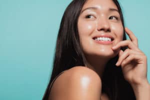 Close up of cute asian girl with glowing skin against blue background. Beautiful face of girl with fresh healthy skin.