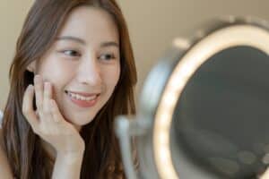 Asian woman sitting in front of mirror applying face cream