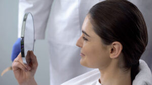 Woman looking at nose in mirror and considering rhinoplasty surgery timing in San Diego, CA
