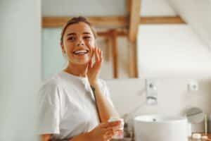 Woman smiling, applying skincare product after Croton Oil Peel in La Jolla, CA