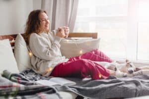 Woman relaxing in bed with tea during facelift recovery in La Jolla, CA